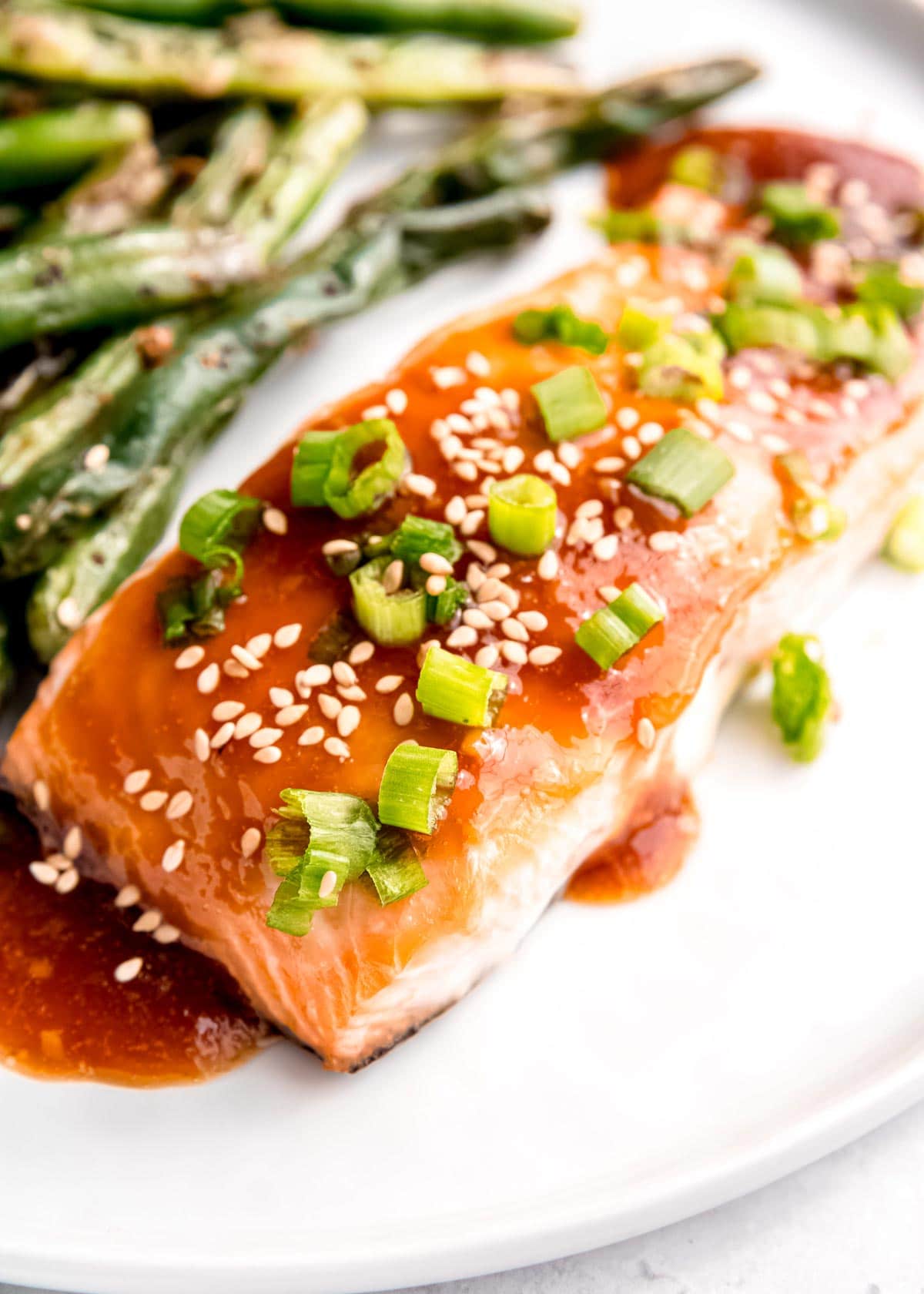 close up image of teriyaki salmon on white plate with green beans in background