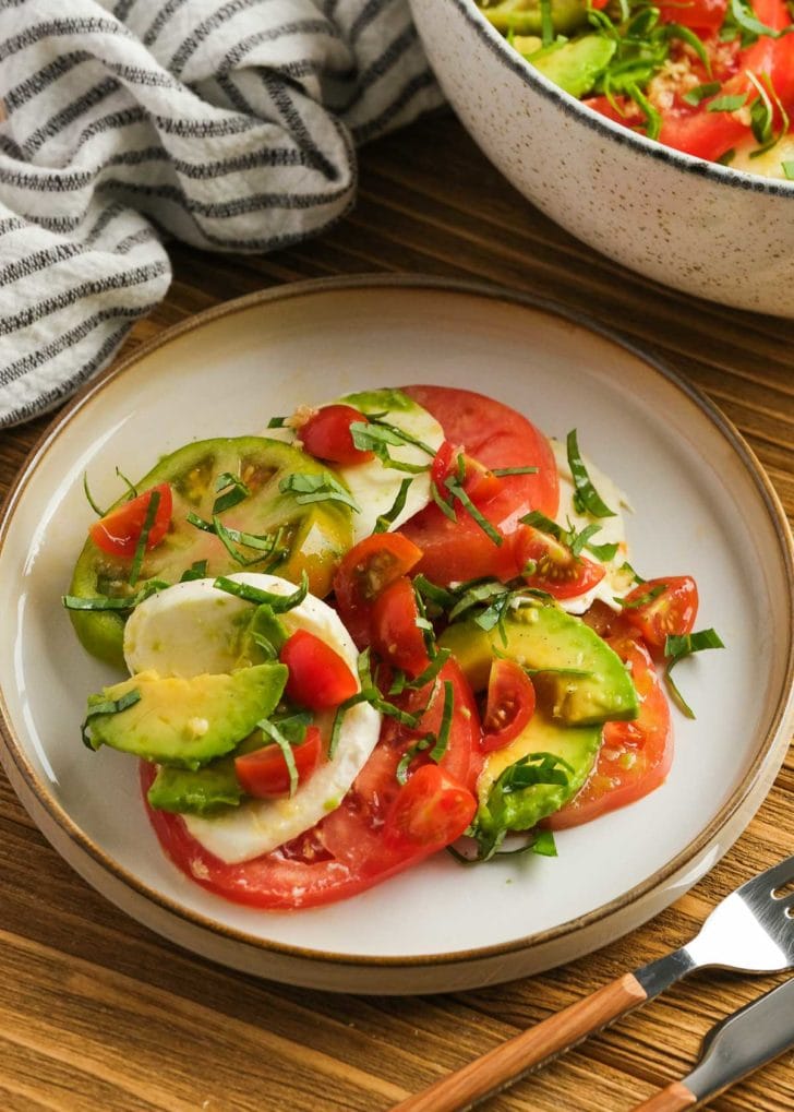 a plate of tomato and avocado salad with mozzarella and basil on a plate