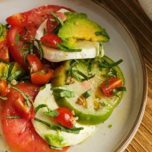 closeup of summer tomato salad with mozzarella, basil, and avocado