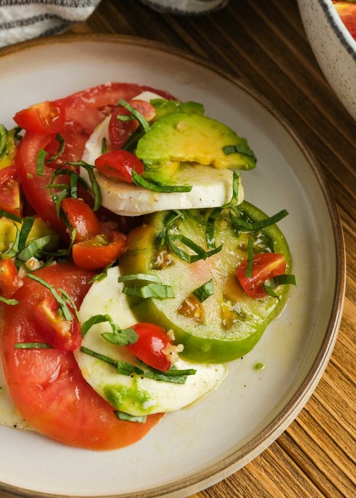 closeup of summer tomato salad with mozzarella, basil, and avocado