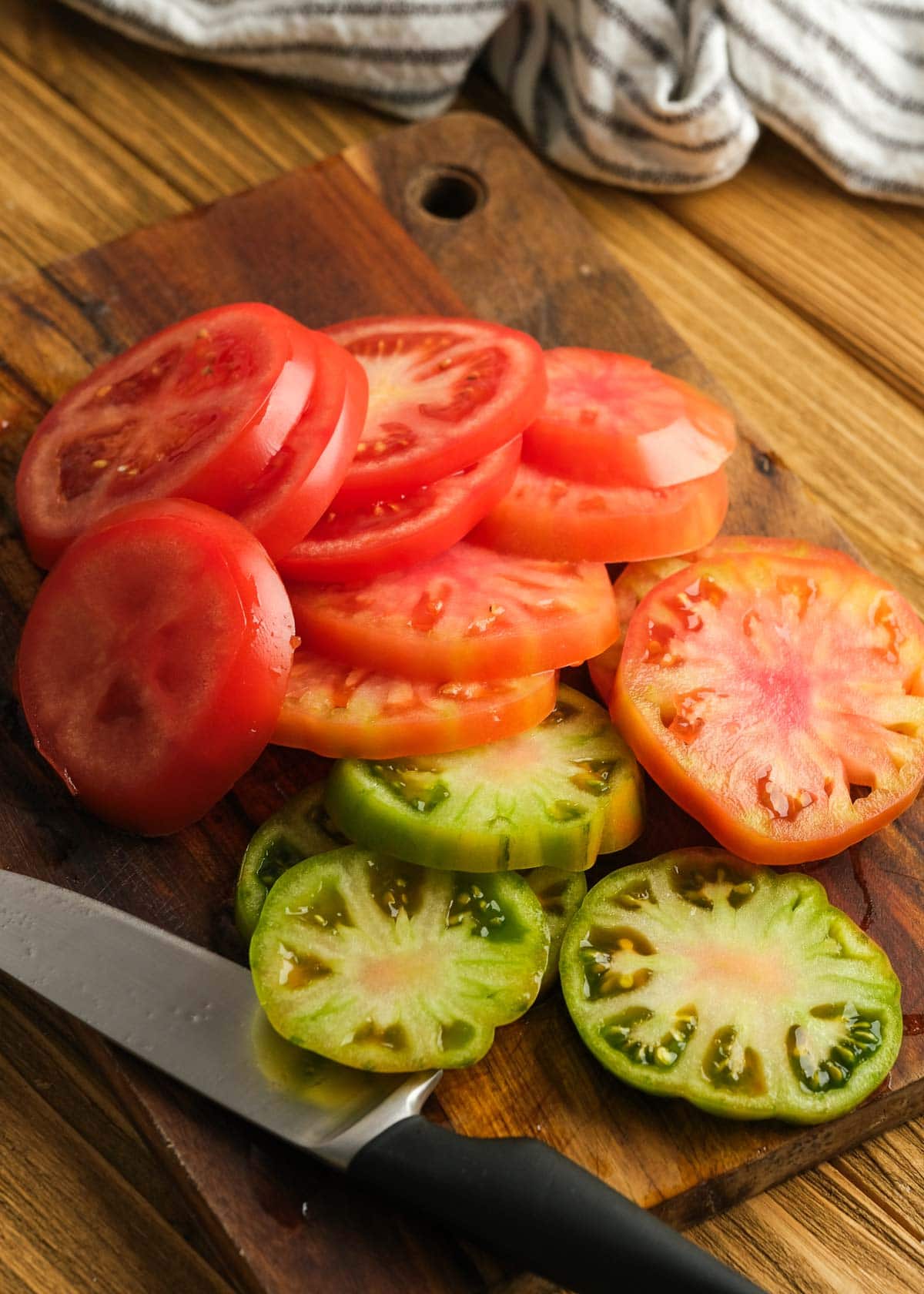 regular and heirloom tomatoes sliced horizontally on a wooden cutting board