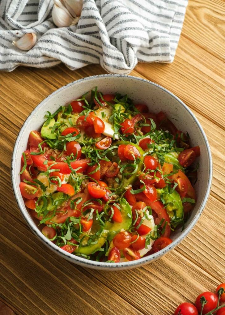 a large bowl full of tomato and avocado salad topped with shredded basil 