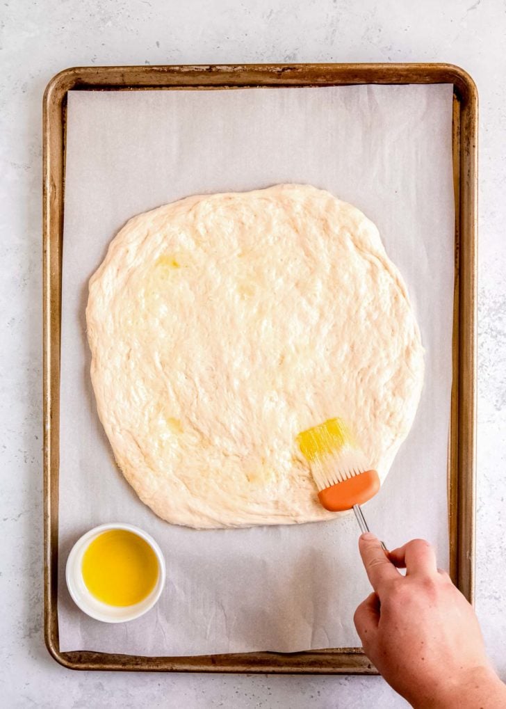 oil being spread on pizza dough on sheet pan