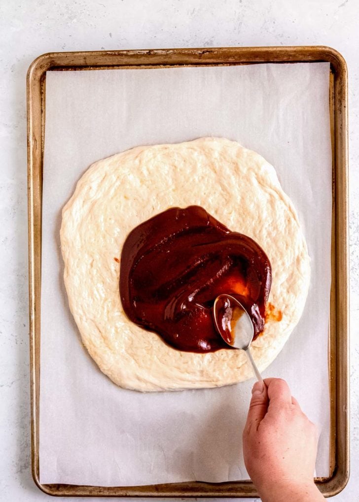 bbq sauce being spread on pizza dough