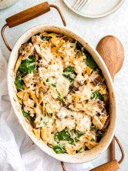 overhead image of baked chicken and mushroom pasta in white dish with wooden spoon on table