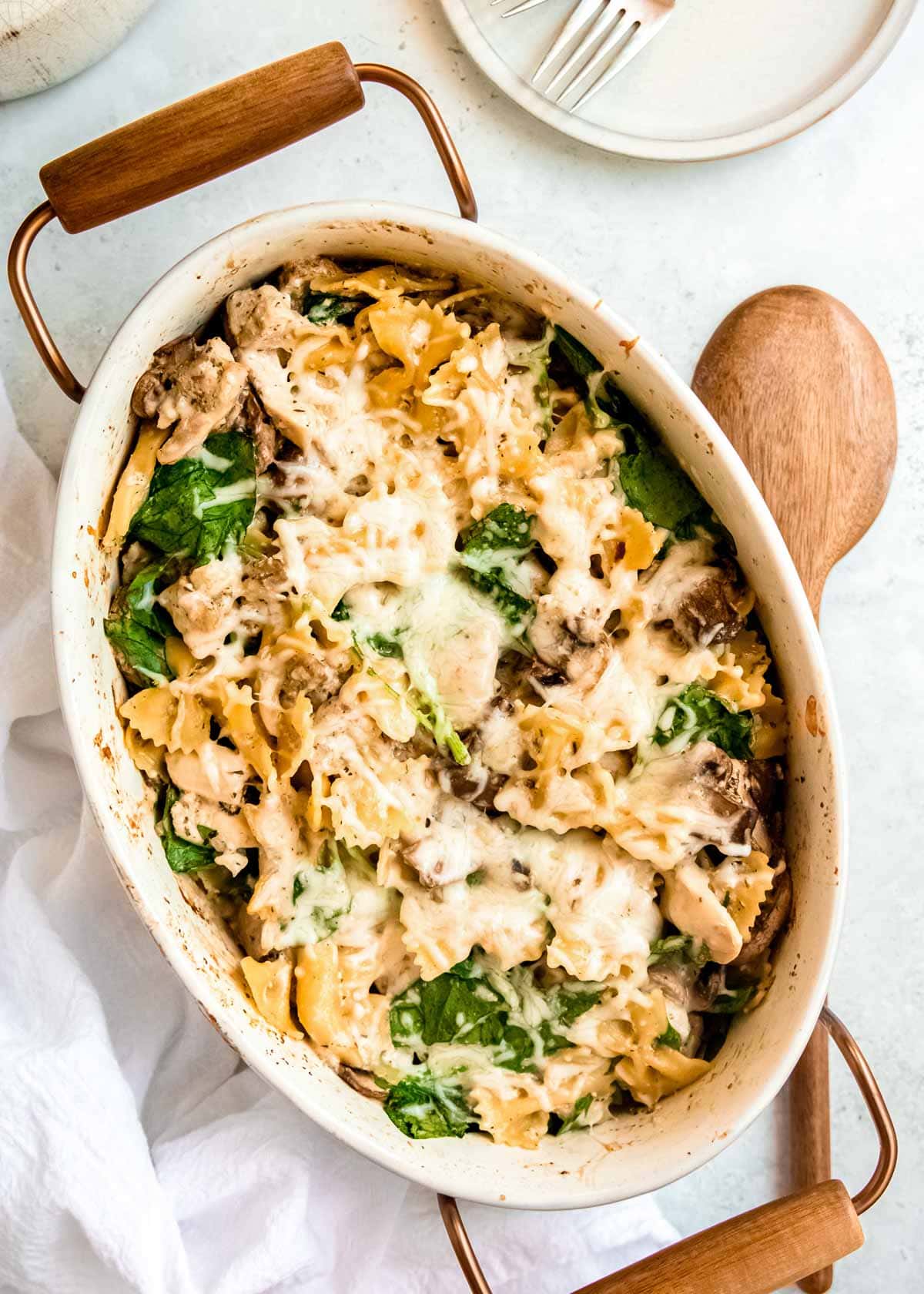 overhead image of baked chicken and mushroom pasta in white dish with wooden spoon on table