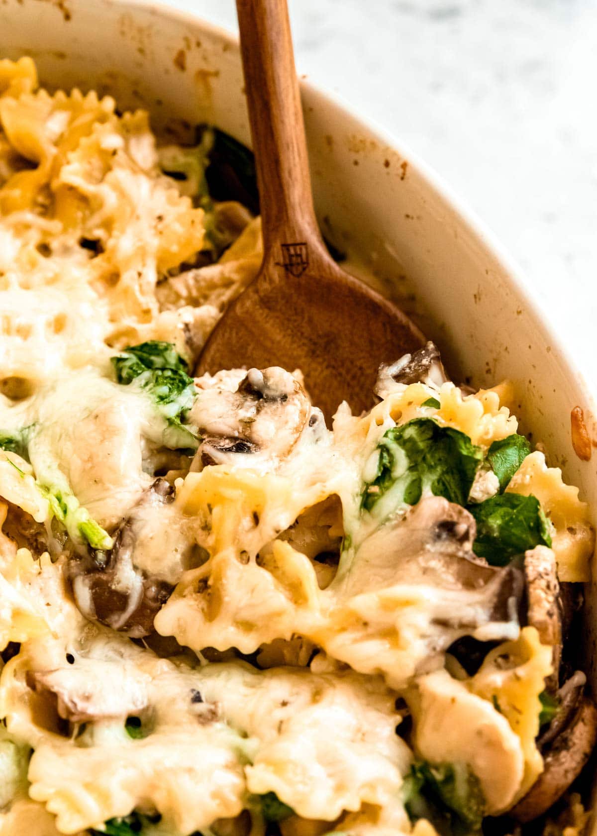 baked chicken and mushroom pasta being scooped out of white baking dish with wooden spoon