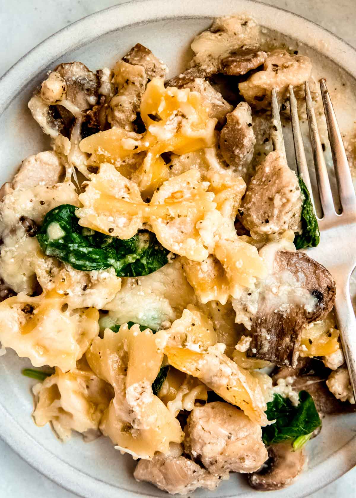 close up image of baked chicken and mushroom pasta on white plate with wooden spoon