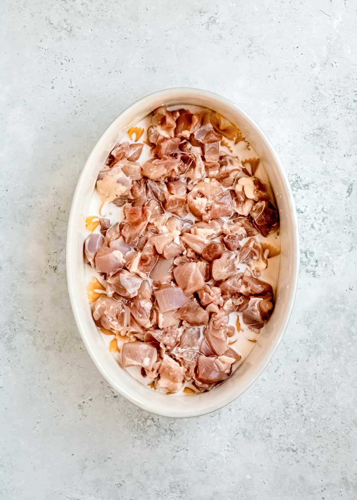 overhead image of raw chicken being added to baking dish with pasta and sauce