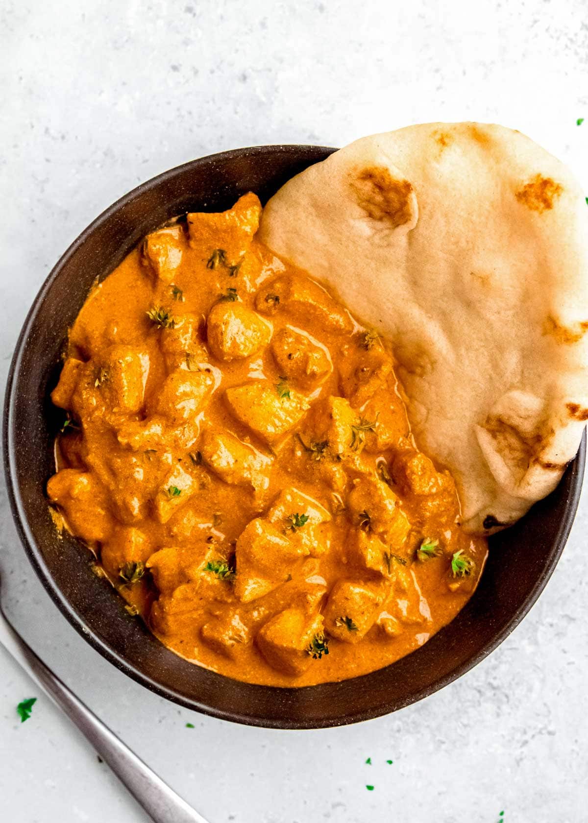 overhead shot showing a black bowl full of creamy butter chicken with a side of naan bread