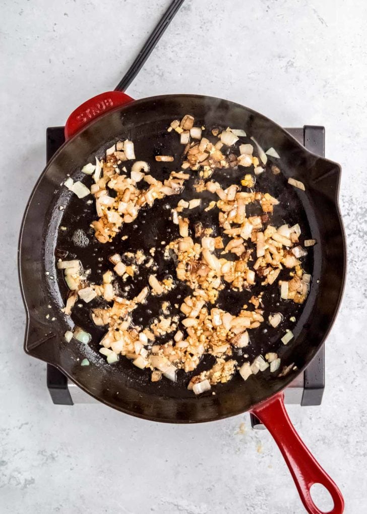 onions, ginger, and garlic being sauteed in skillet