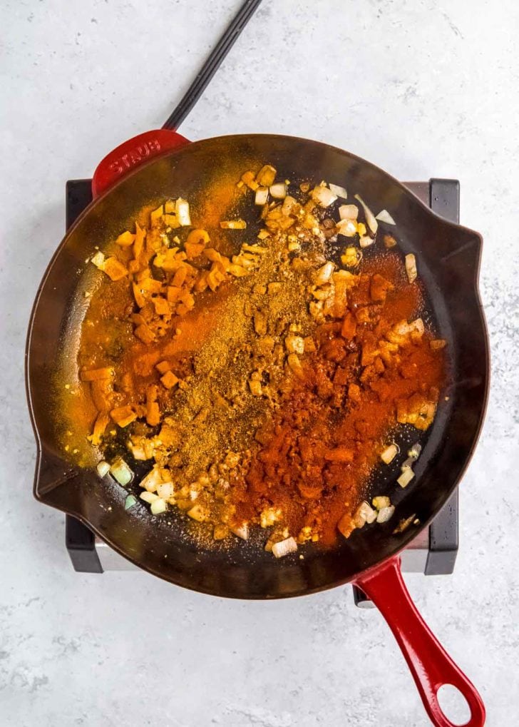 spices being added to skillet with onion, ginger, and garlic