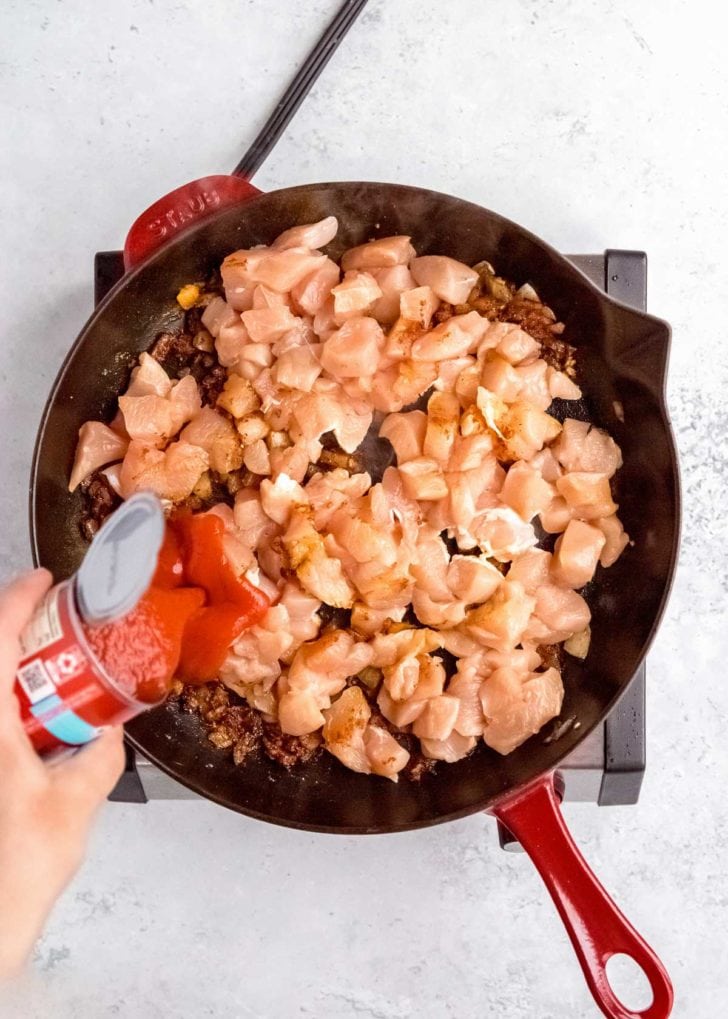 raw chicken being added to skillet with other butter chicken ingredients