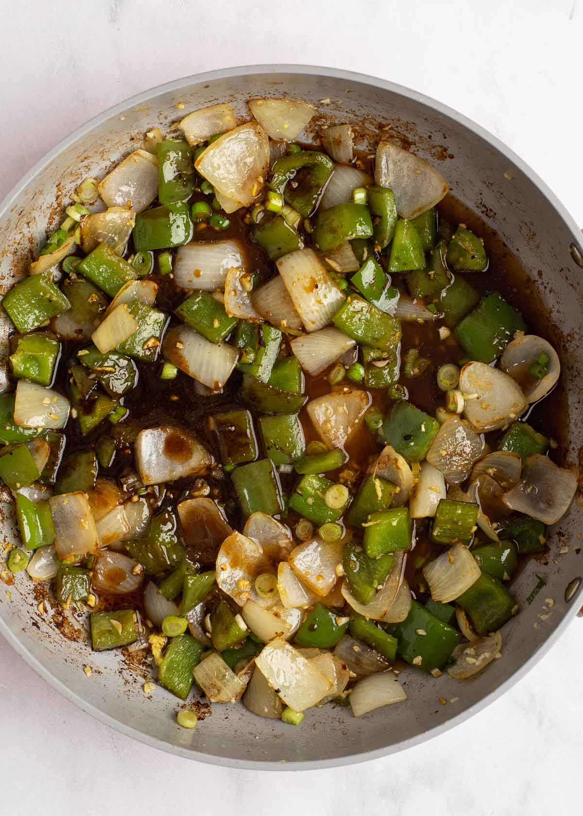 sauce being added to vegetables in a gray skillet