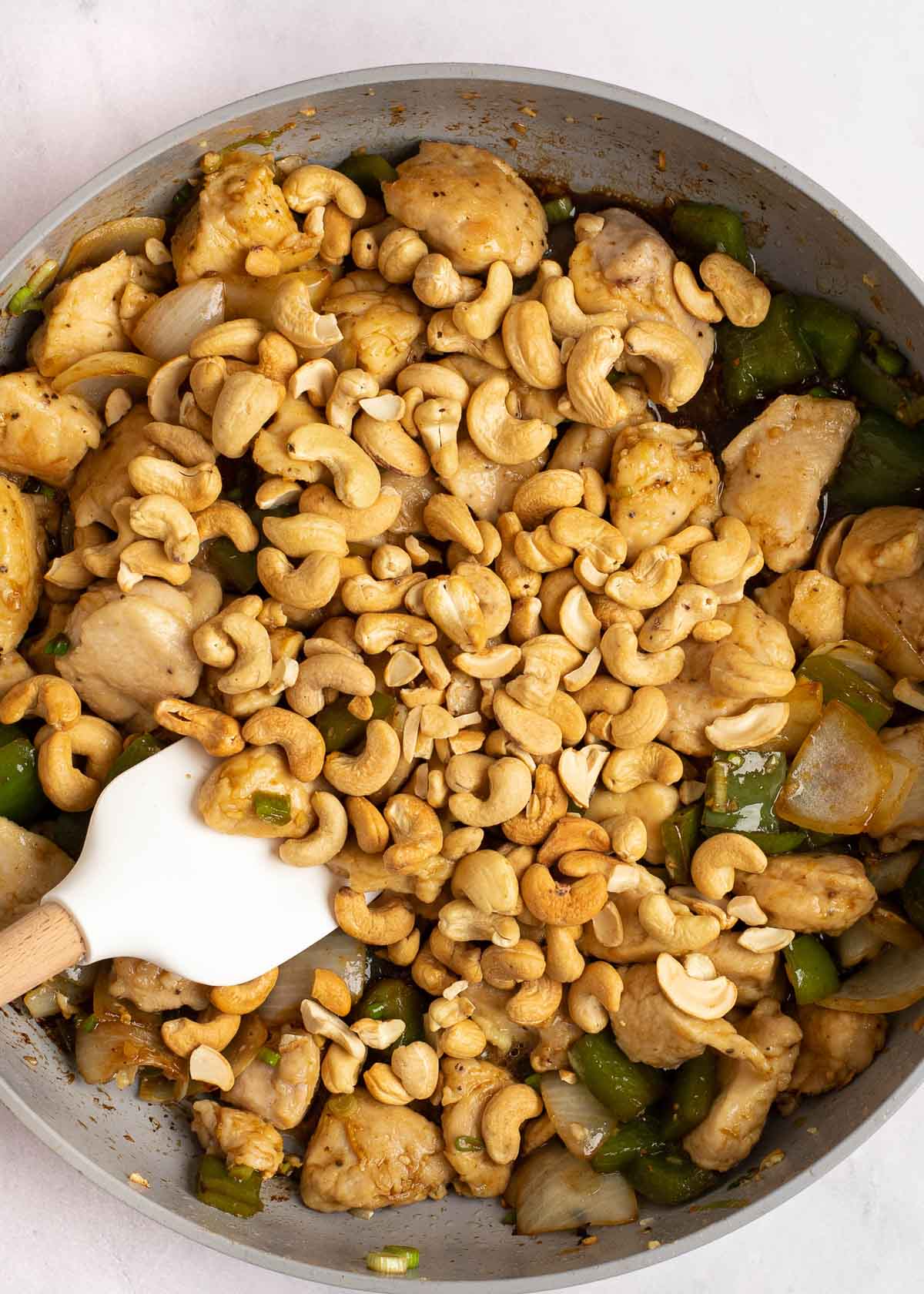 cashews being added to cashew chicken in a skillet