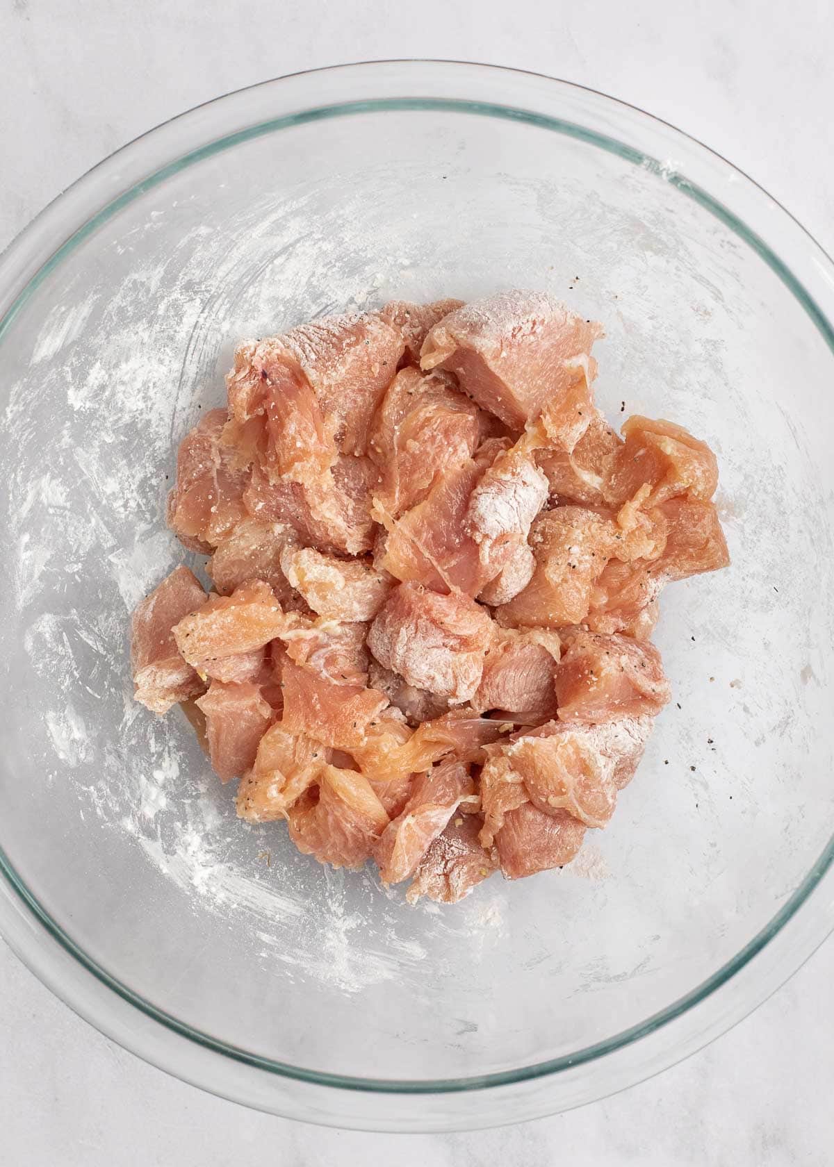 seasoned raw chicken in clear mixing bowl