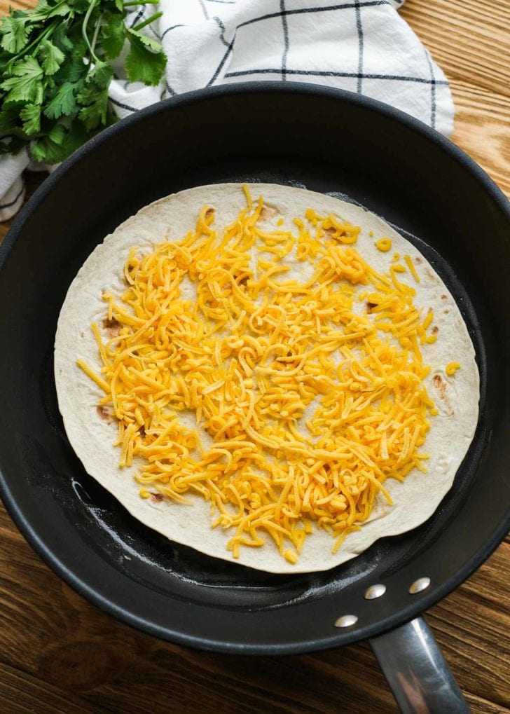 shredded cheese on tortilla in a skillet