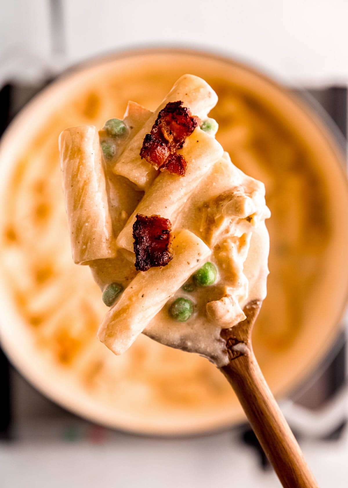 a spoonful of creamy pasta with chicken, bacon, peas, and carrots over a pot full of pasta