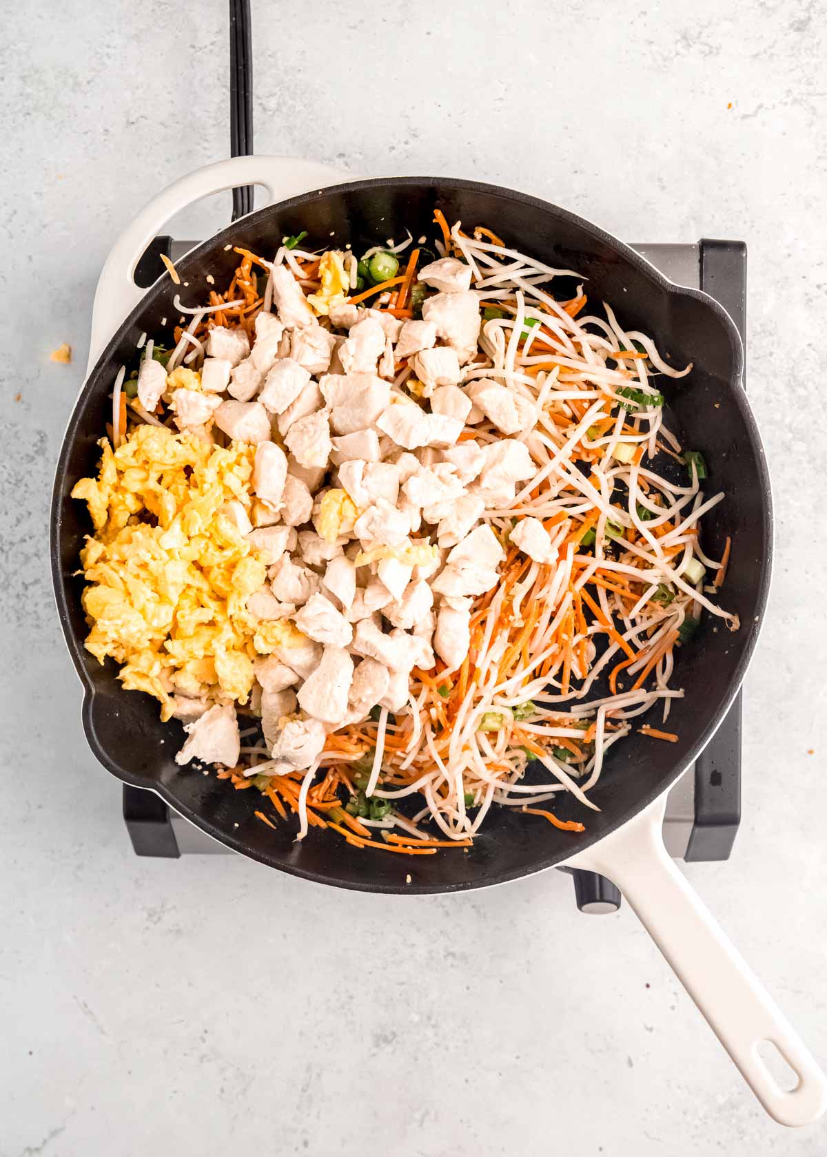 overhead image of chicken being added to vegetables in skillet