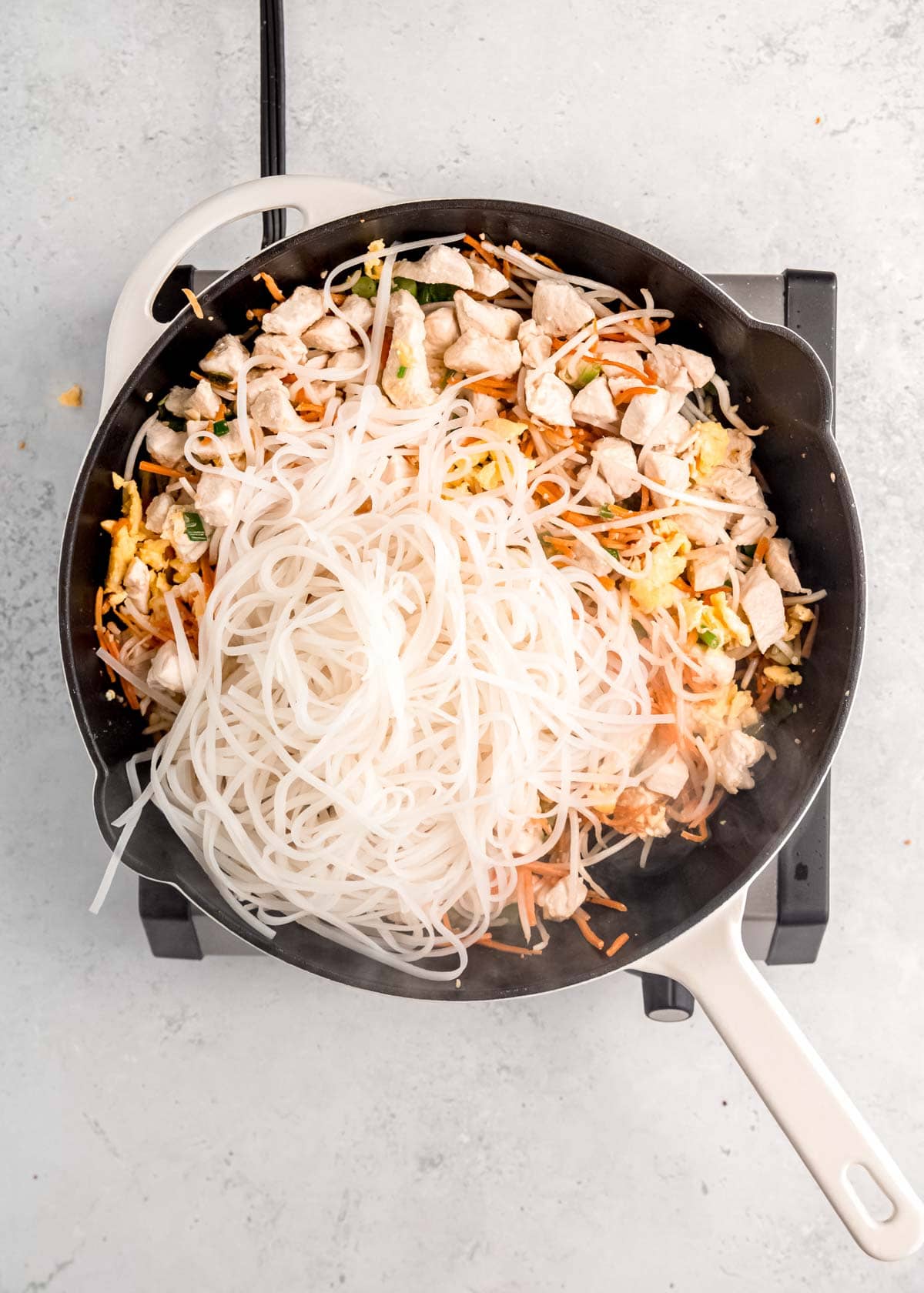 noodles being added to skillet with chicken and vegetables 