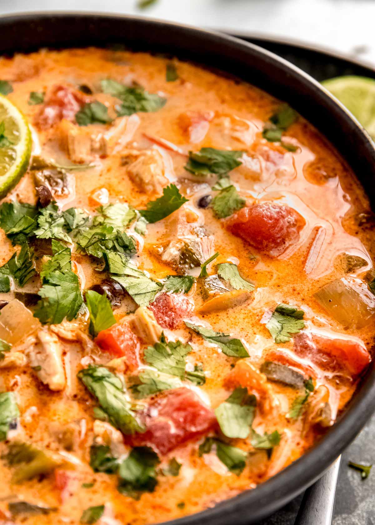 closeup view of a dark bowl of creamy chicken poblano soup garnished with fresh herbs and a lime slice