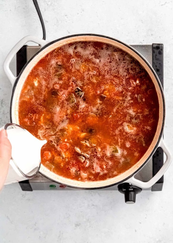 cream being poured into dutch oven with other chicken poblano soup ingredients 