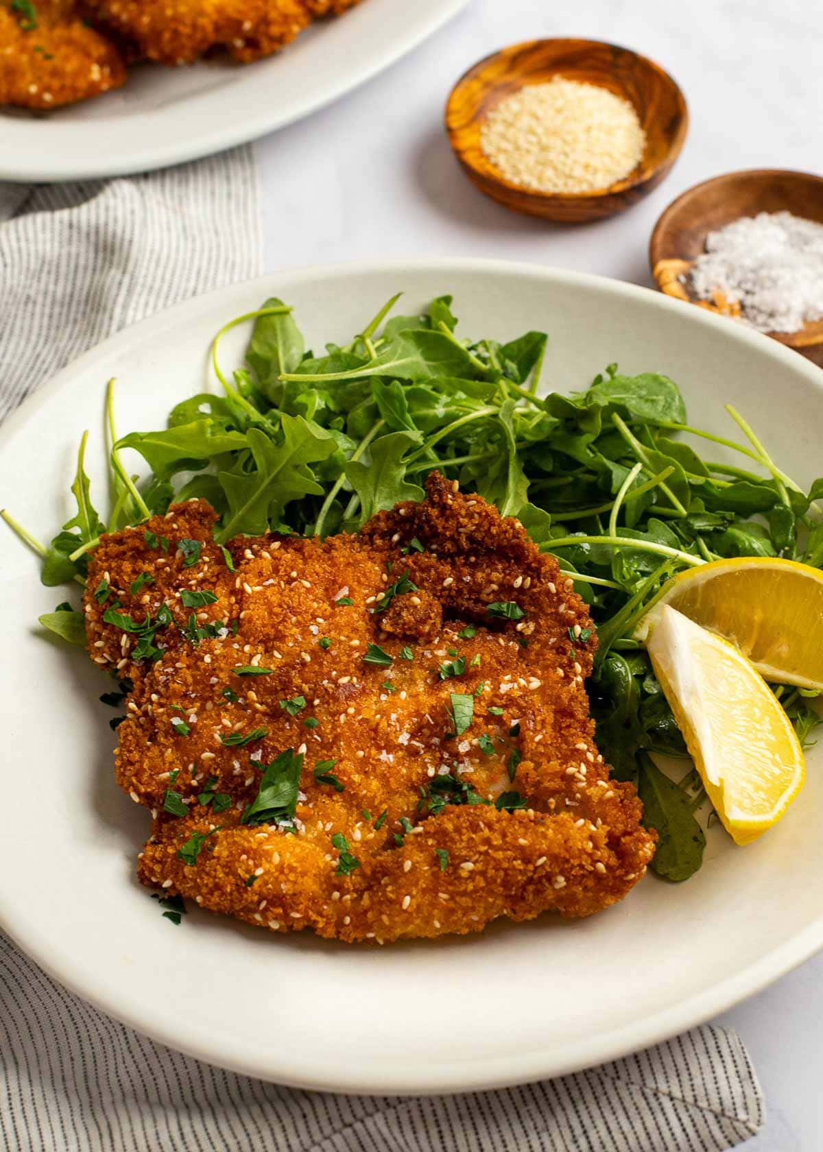 a white plate topped with a green salad, a fried chicken schnitzel cutlet, and lemon wedges on the side