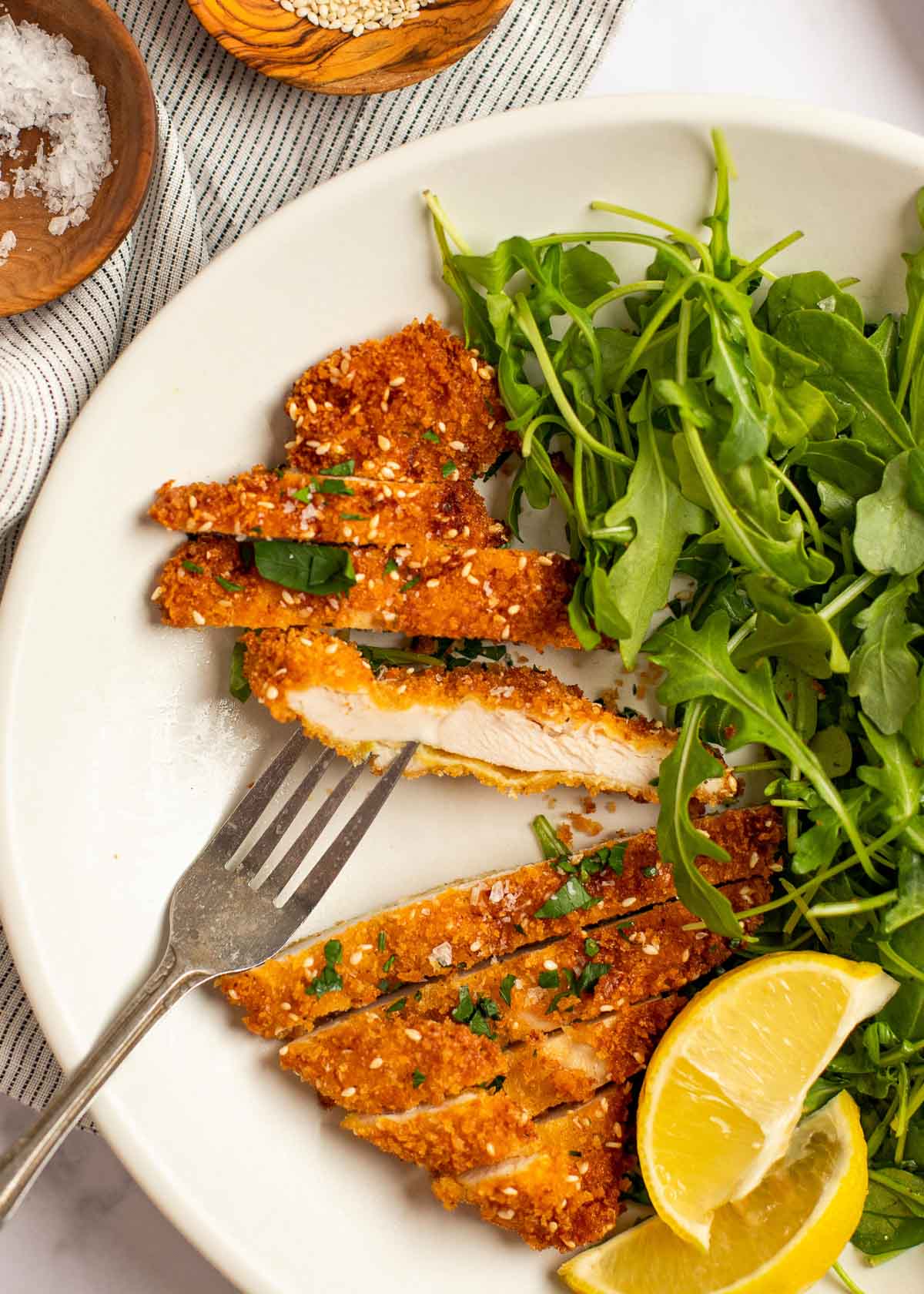 juicy sliced chicken schnitzel with a side of lemon wedges and a simple salad