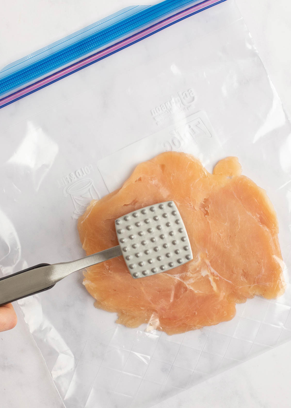 chicken being tenderized on white table 