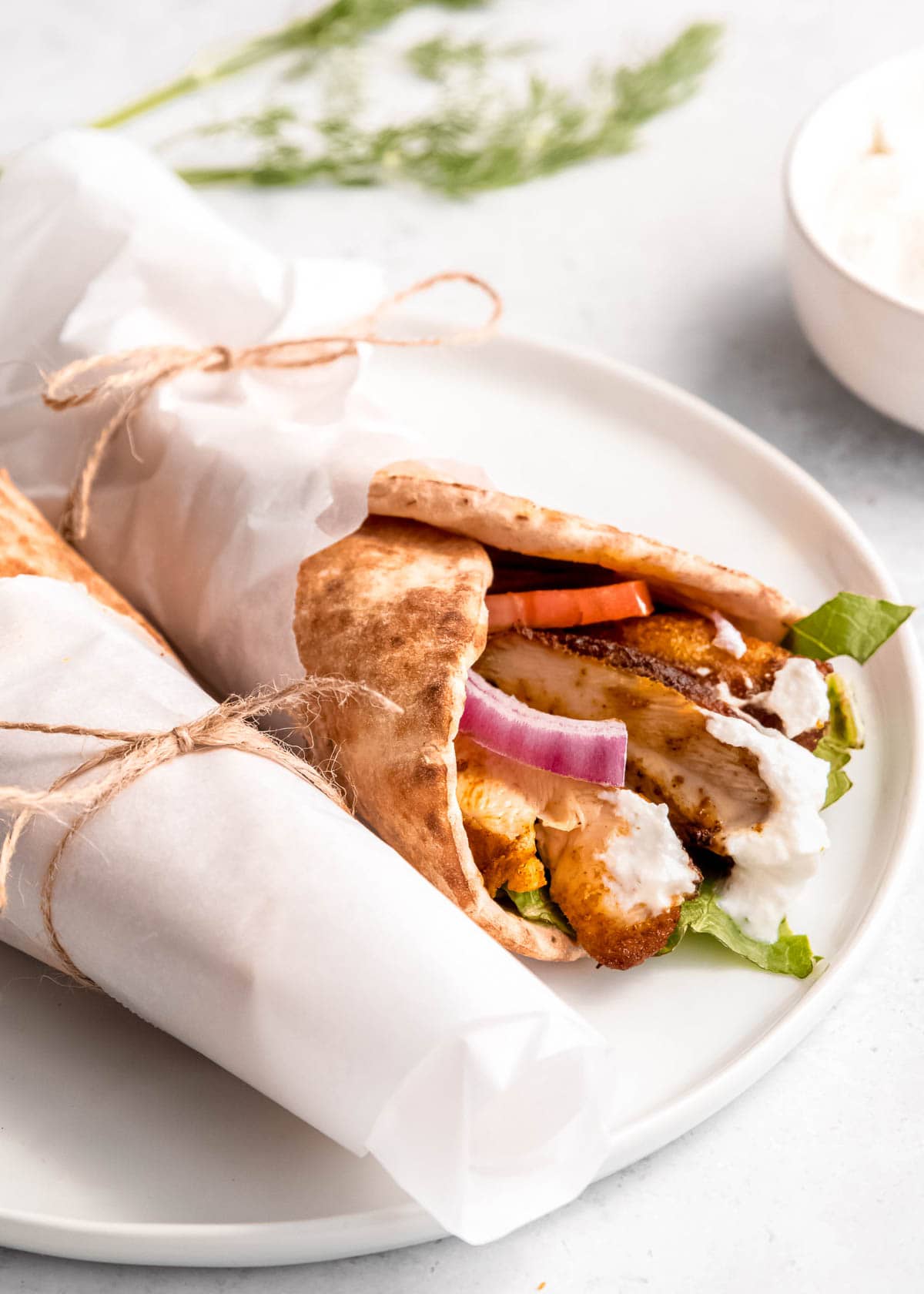 two chicken shawarma pita wraps wrapped in parchment paper on a white plate