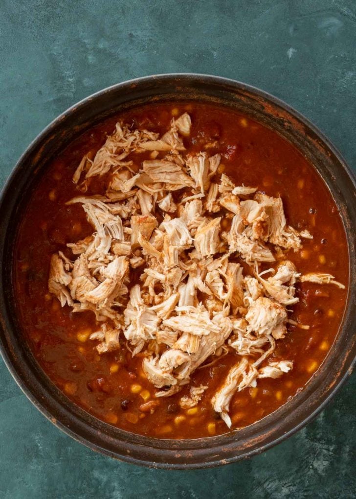 shredded chicken on top of chicken tortilla soup in black dutch oven