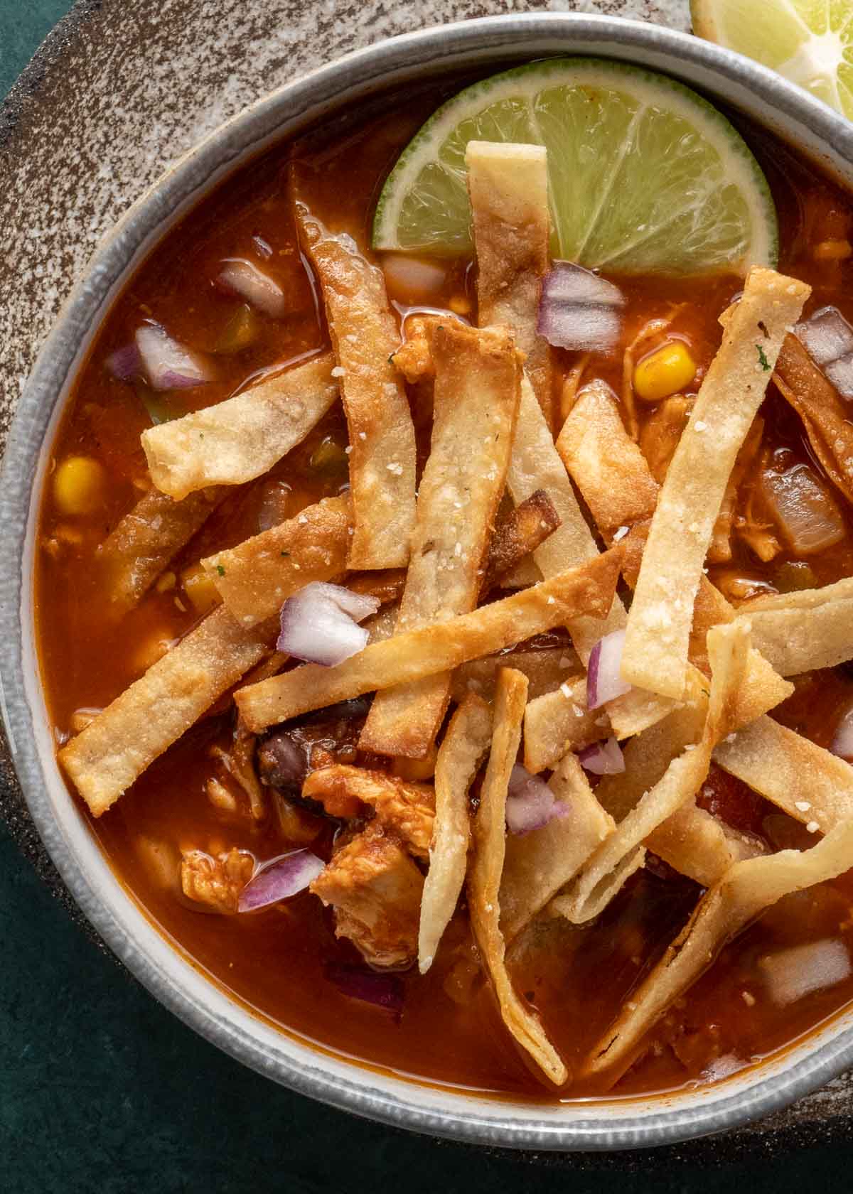 closeup of chicken tortilla soup topped with a lime wedge and tortilla strips