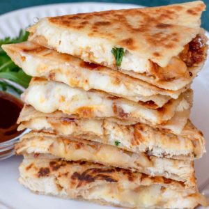 close up bbq chicken quesadilla slices stacked on a white plate