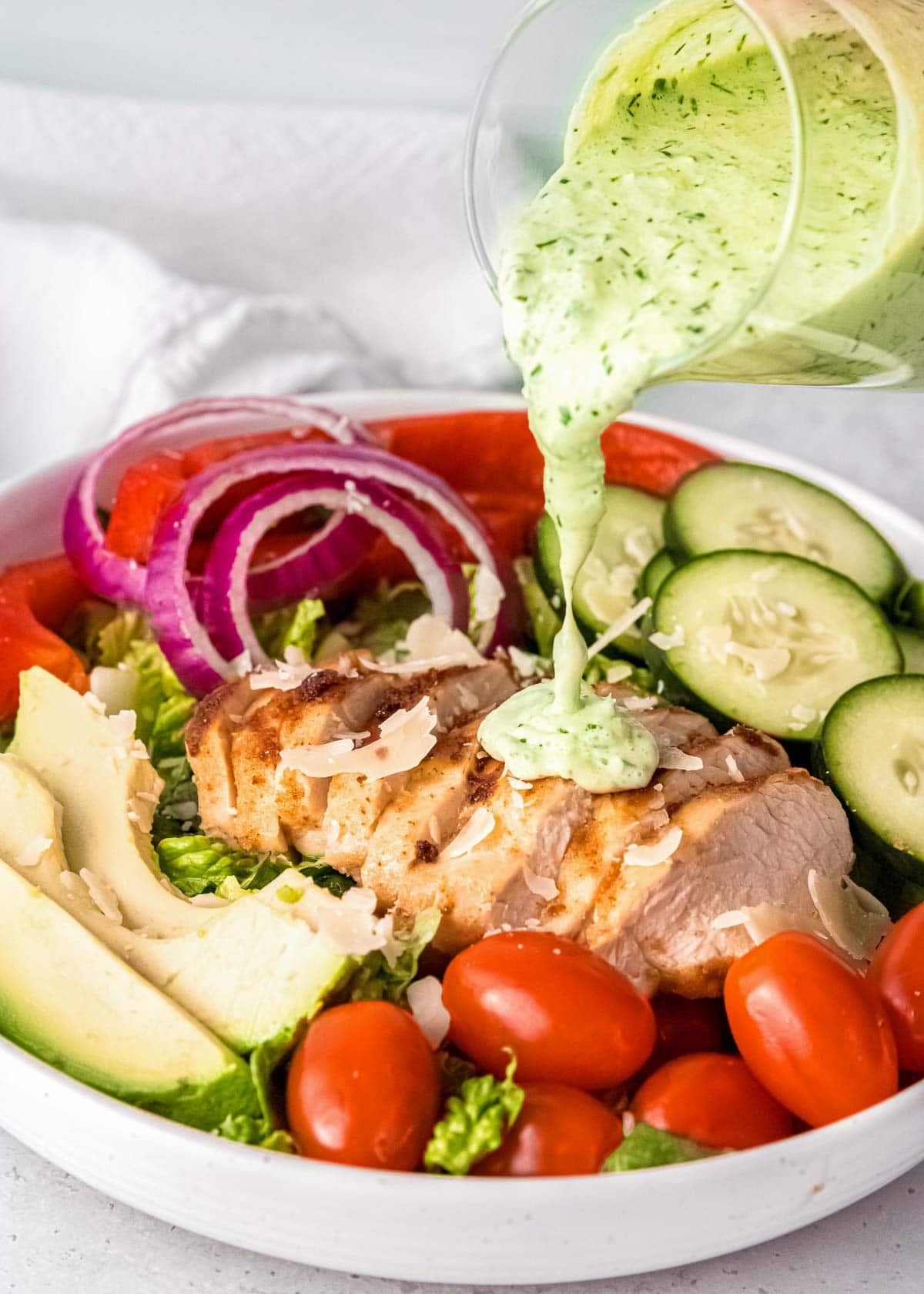 green goddess dressing being poured on chicken on white plate