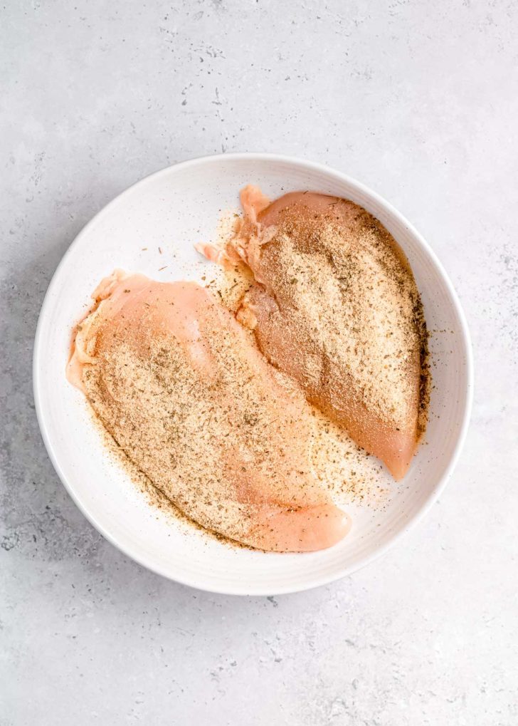 raw chicken breast and seasoning in white bowl