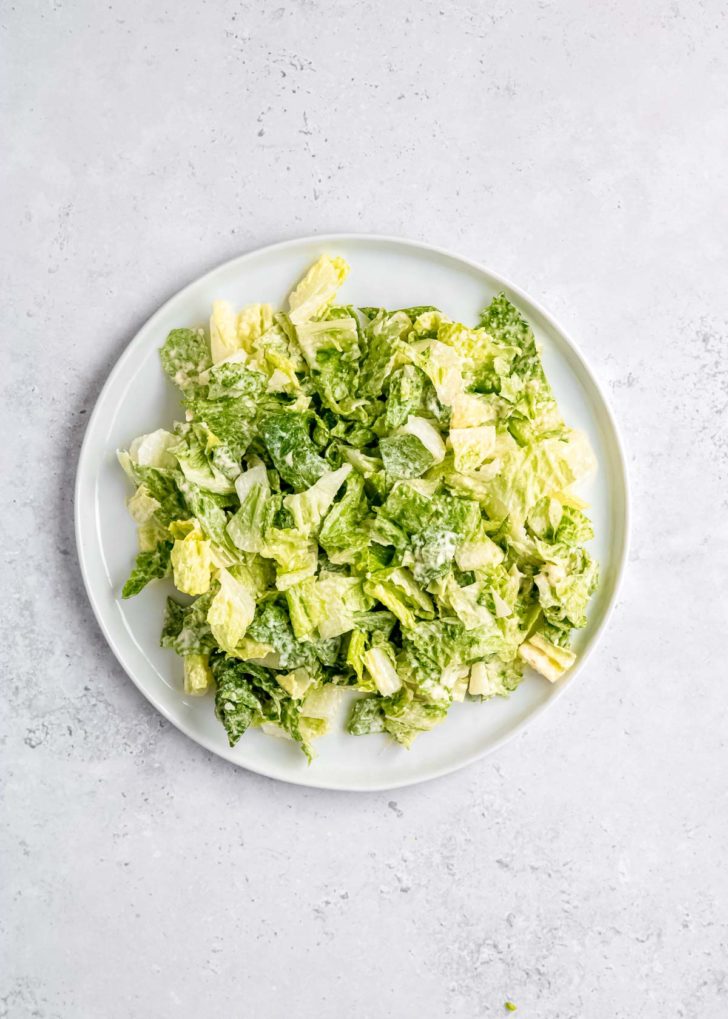 lettuce with caesar salad mixed together in white bowl