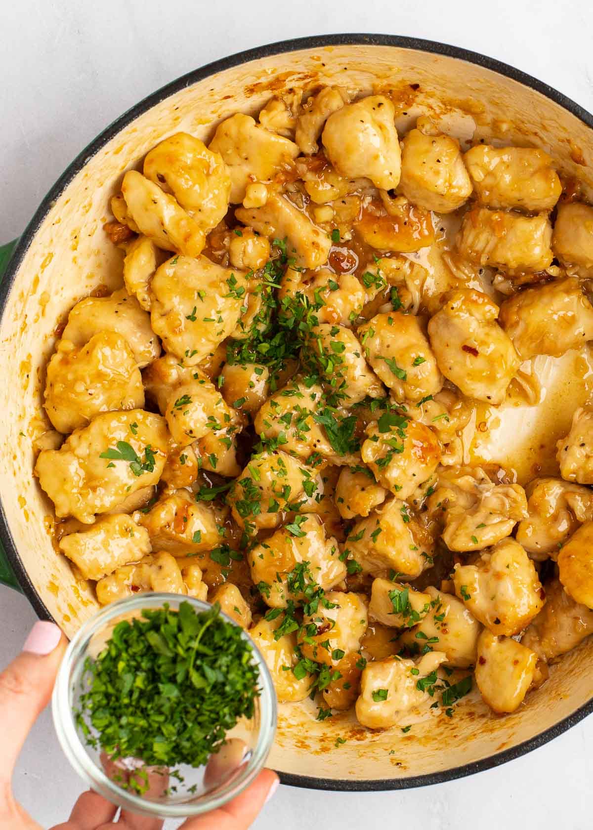 parsley being added to honey garlic chicken in dutch oven