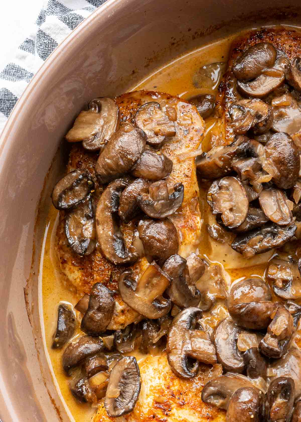 four chicken breasts in a skillet smothered in creamy mushroom sauce