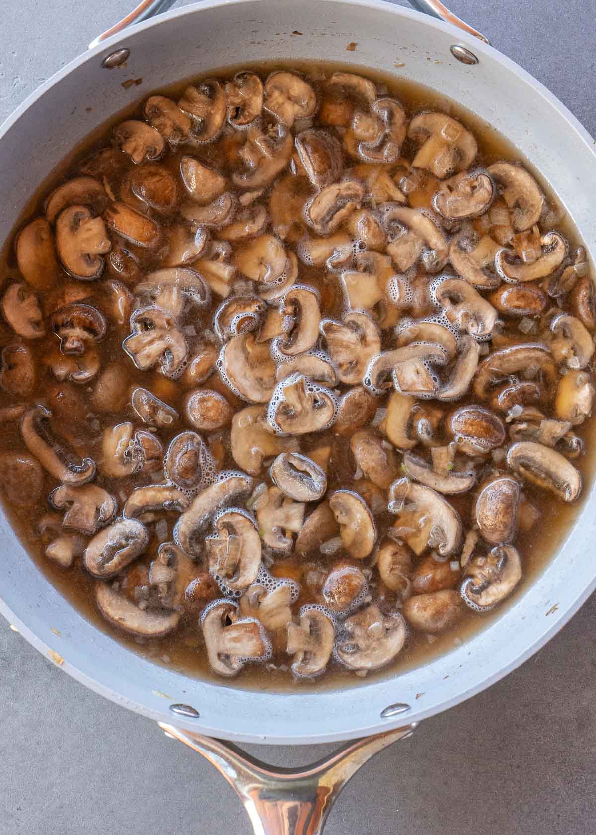 cooked mushrooms, broth, and wine in a skillet