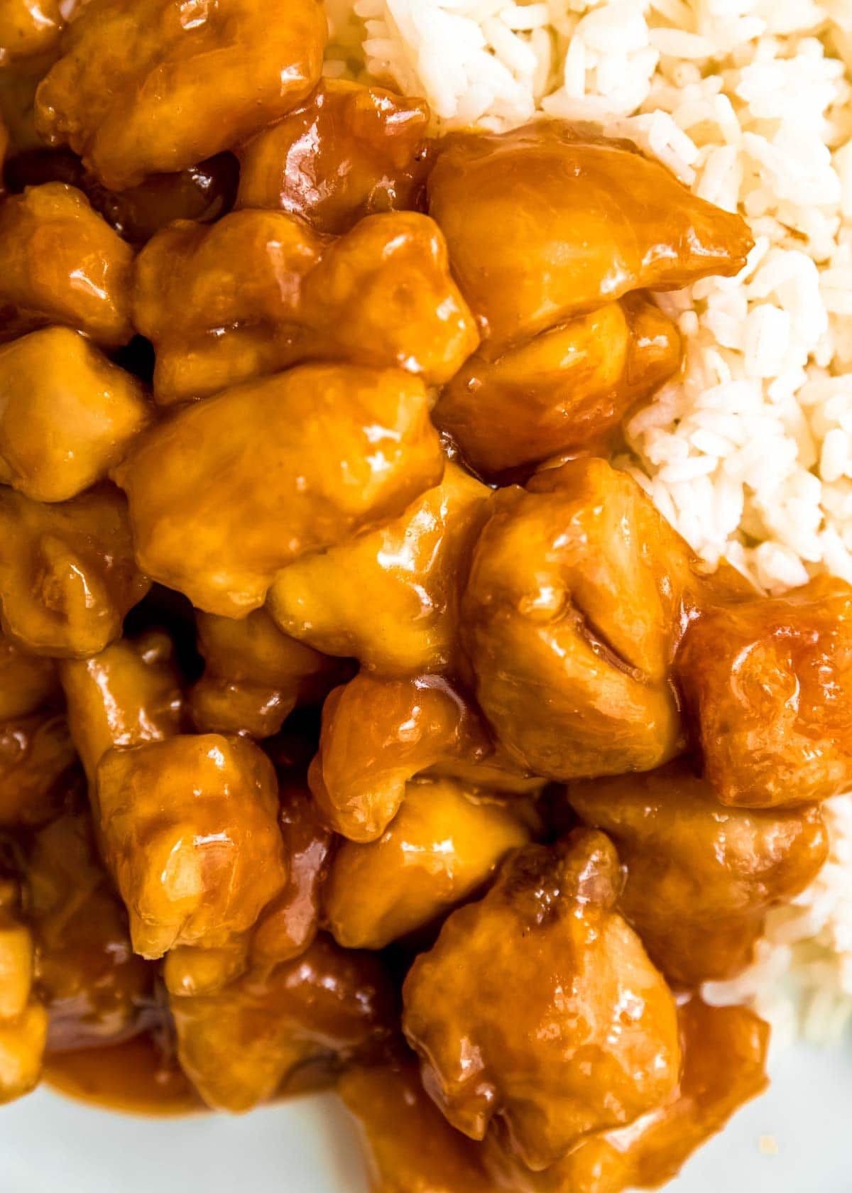 closeup view of crispy fried chicken covered in sticky sweet orange sauce with a side of rice