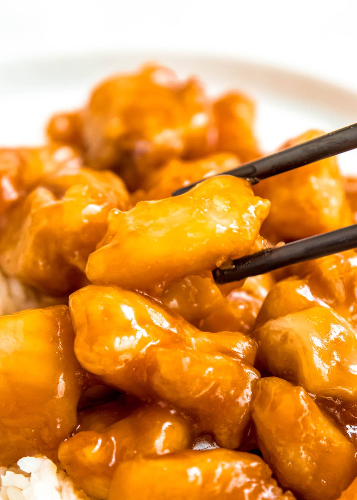 close up image of orange chicken being picked up with chopsticks