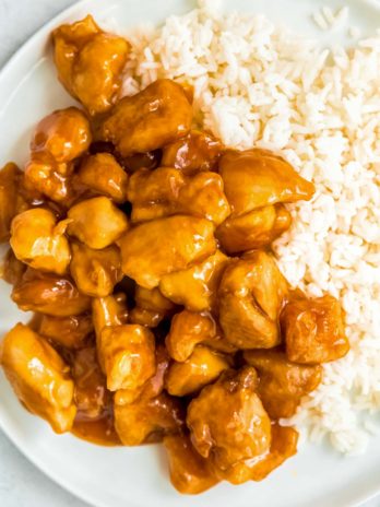 close up, overhead image of orange chicken and rice on white plate