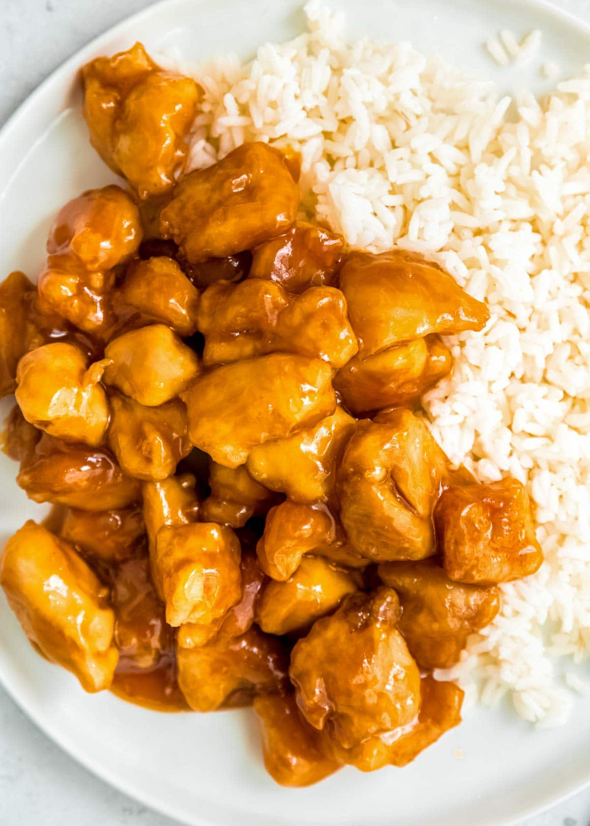 close up, overhead image of orange chicken and rice on white plate