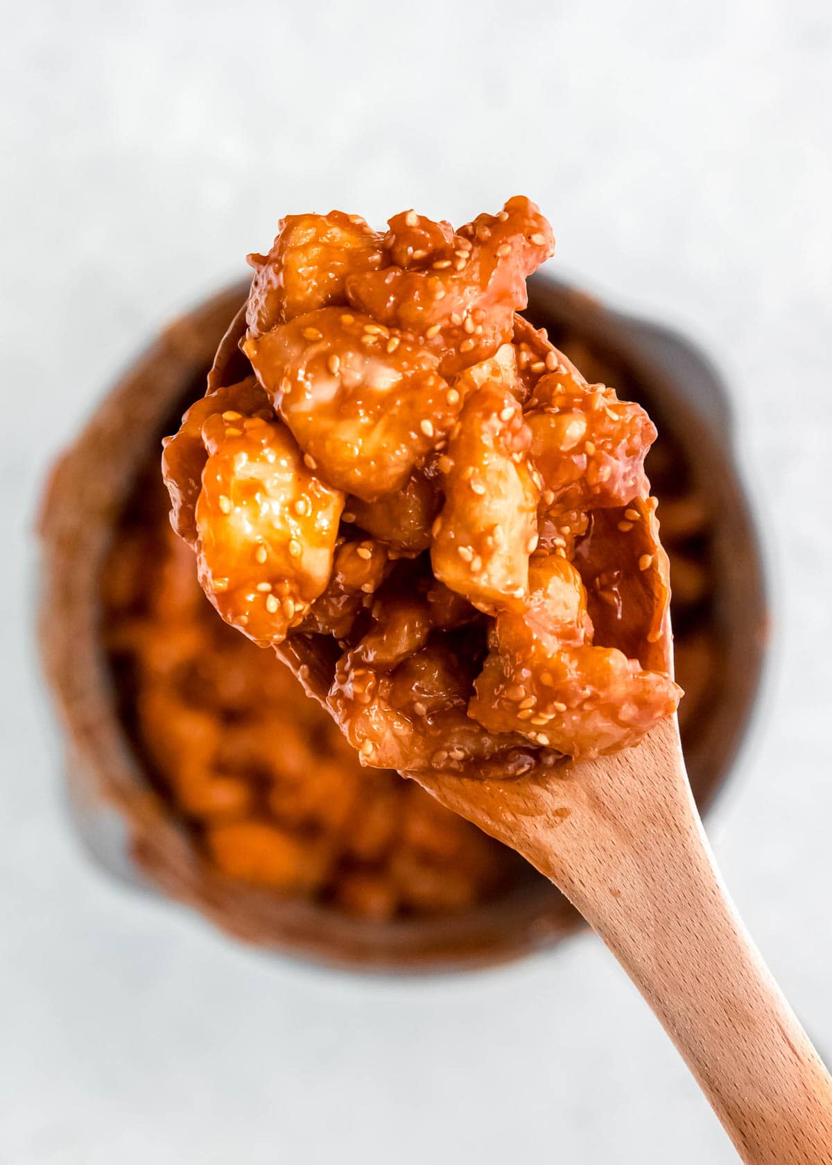 sesame chicken covered in sauce on wooden spoon