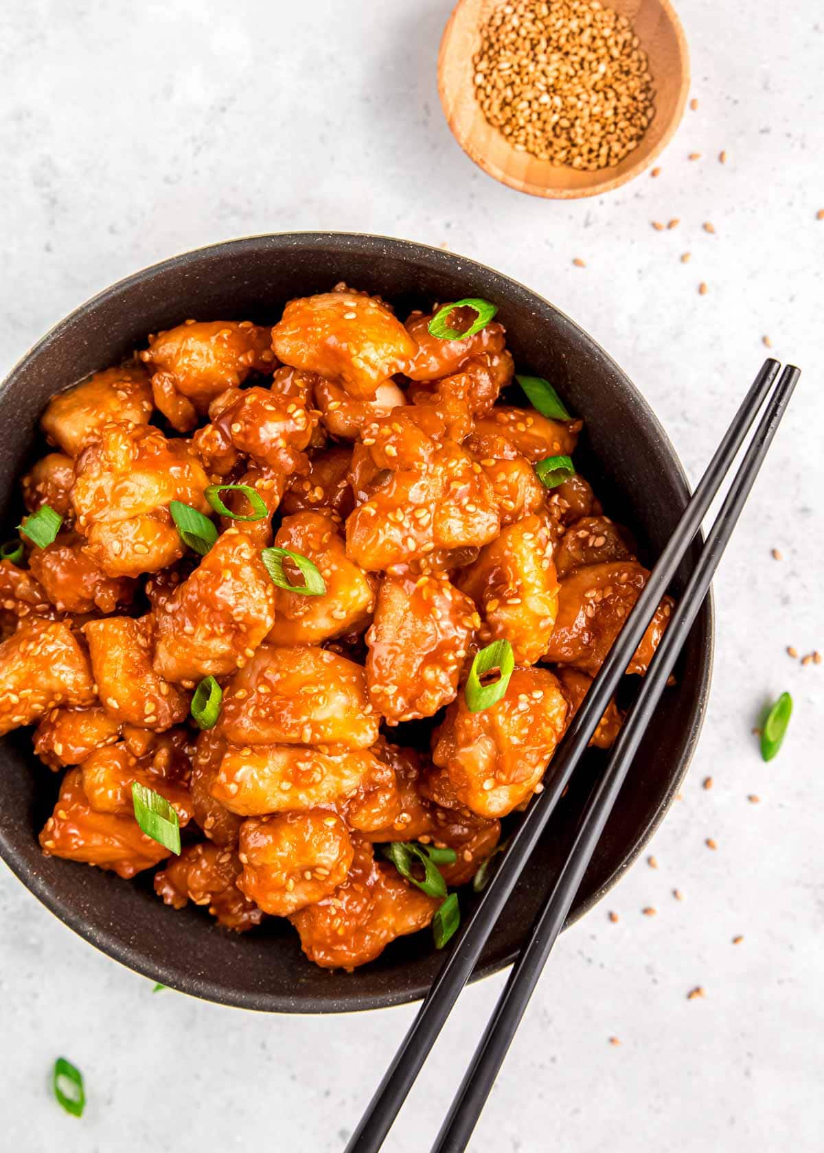 overhead image of sesame chicken and chopsticks in black bowl