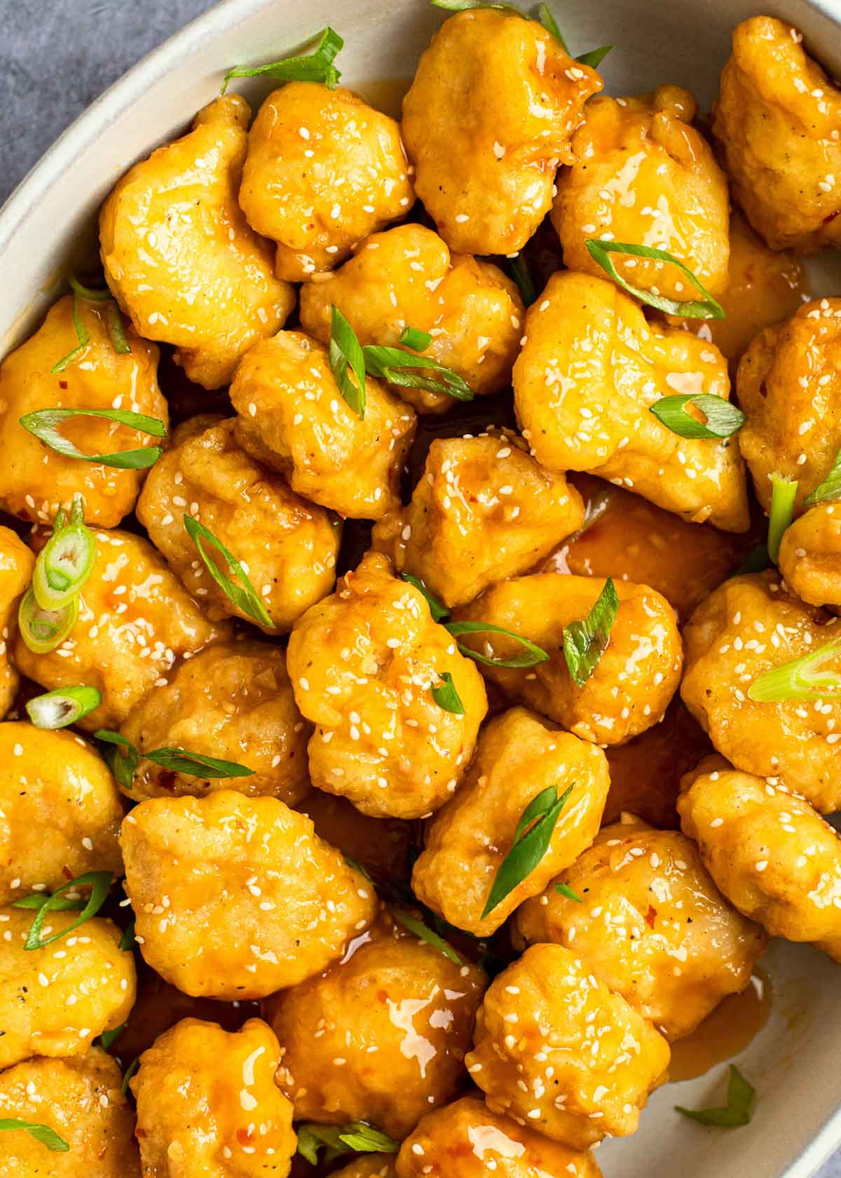 a white dish filled with sweet and sour chicken topped with fresh scallions