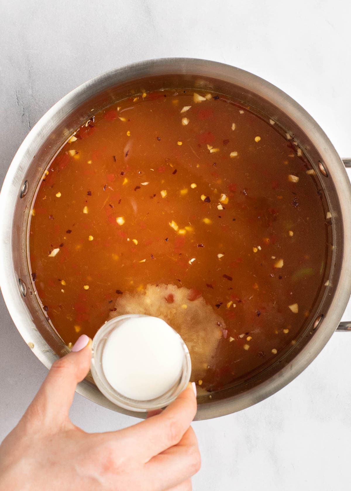 cornstarch slurry being added to sweet and sour sauce