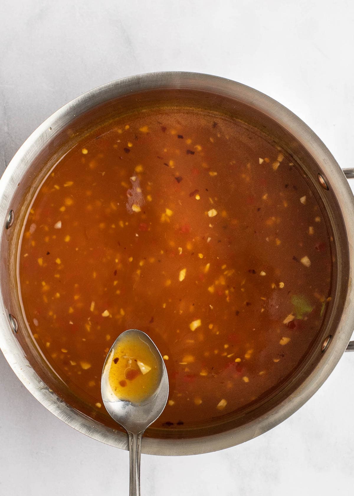 sweet and sour sauce being spooned out of sauce pan