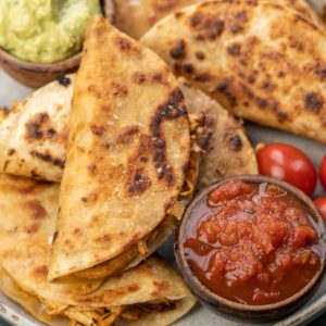 close up image of chicken tacos stacked on plate with avocado