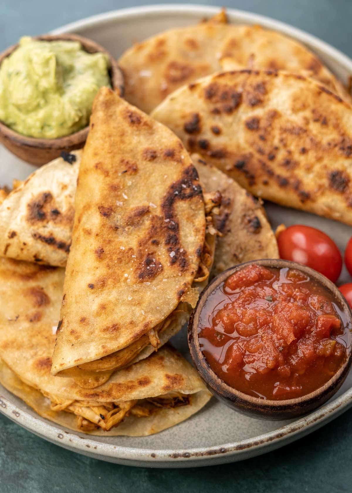 close up image of chicken tacos stacked on plate with avocado